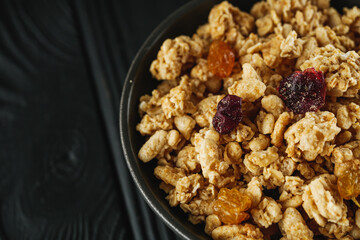 tasty crunchy granola with dried fruits on a black wooden rustic background