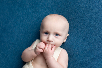 small child with fingers in mouth on blue background. portrait of a newborn boy. baby's first photo...