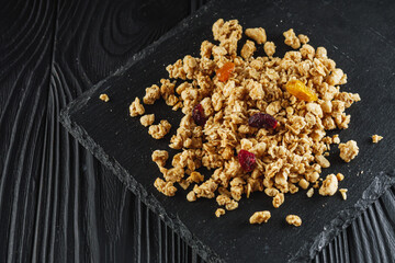tasty crunchy granola with dried fruits on a black wooden rustic background