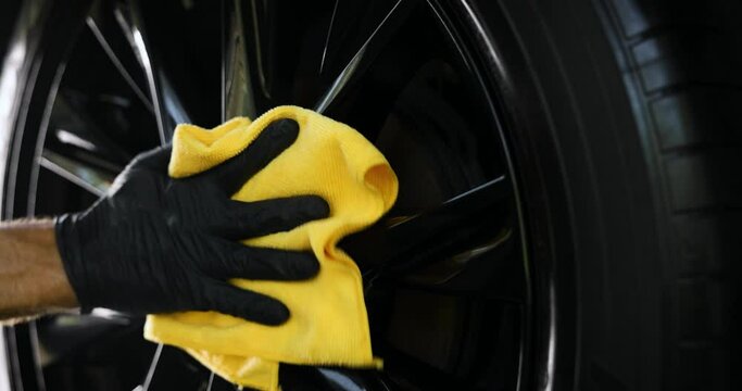 car detailing. hand is cleaning a black shiny alloy wheel with microfiber cloth