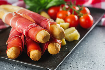 crispy grissini with prosciutto on a light stone background