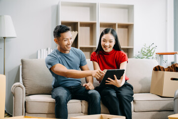 Asian young attractive couple man and woman use tablet and smartphone online shopping furniture decorate house with carton package move in new house. married asian moving home. .