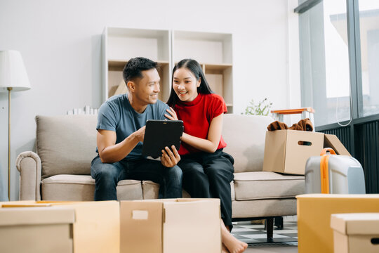 Asian young attractive couple man and woman use tablet and smartphone online shopping furniture decorate house with carton package move in new house. married asian moving home. .