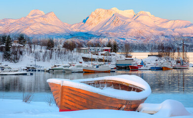 Fisher shelter in winter with fishboat at sunset in the background snowy mountains and Norwegian...