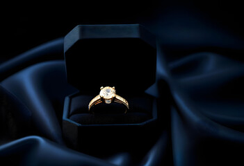 A close-up of a gold ring in a velvet jewelry box on a dark blue background