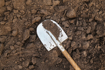 Brown soil ground texture with shovel on garden bed in farm garden close up top view. Organic...