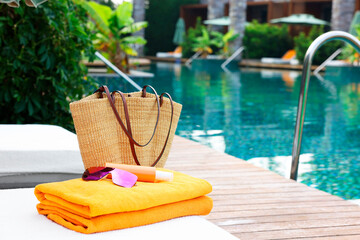 Wicker bag with beach accessories on sunbed near outdoor swimming pool, space for text. Luxury resort