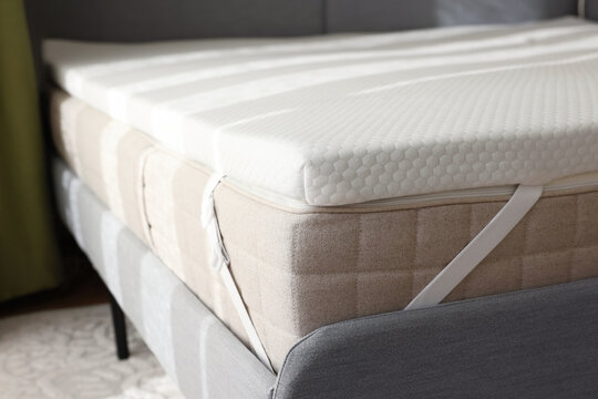 White memory foam mattress topper on grey bed indoors, closeup