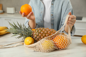 Woman with string bag of fresh fruits at light marble table, closeup