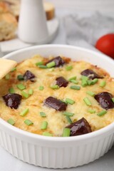 Tasty sausage casserole with green onions in baking dish served on white table, closeup