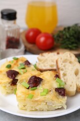 Tasty sausage casserole with green onion and bread on grey table, closeup