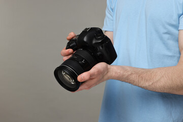 Photographer holding camera on grey background, closeup. Space for text