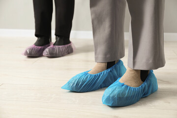 Women wearing blue shoe covers onto different footwear indoors, selective focus