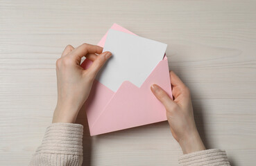 Woman taking card out of letter envelope at light wooden table, top view