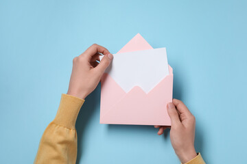 Woman taking card out of letter envelope at light blue table, top view