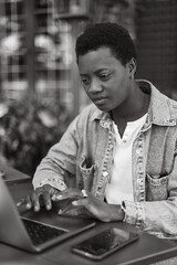 Young black person with afro hairstyle, denim jacket at cafe terrace, work online, talk and gesture