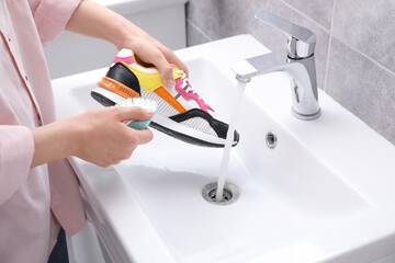 Woman washing stylish sneakers with brush in sink, closeup