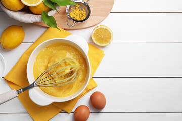 Delicious lemon curd in bowl, ingredients, whisk and sieve on white wooden table, flat lay. Space...