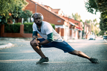African American man stretching during street workout with headphones