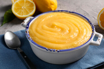 Delicious lemon curd in bowl, fresh citrus fruits and spoon on grey table, closeup