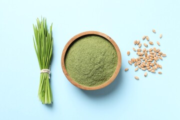 Wheat grass powder in bowl, seeds and fresh sprouts on light blue background, flat lay