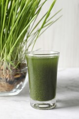Wheat grass drink in shot glass and fresh sprouts on white marble table, closeup