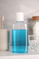 Bottle of mouthwash, toothbrush and cotton buds on white shelf in bathroom