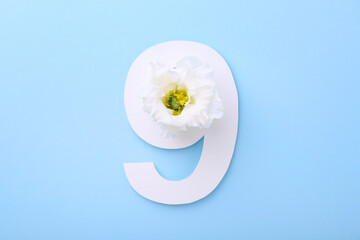 Paper number 9 and beautiful flower on light blue background, top view