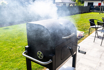 Thick smoke rising from a modern grill standing on a paving slab on the terrace.