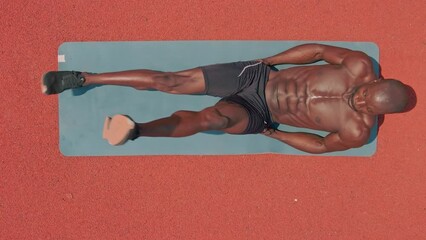 Top view of African ethnicity muscle man training abdominals outside on a yoga matt with a red background. - Powered by Adobe