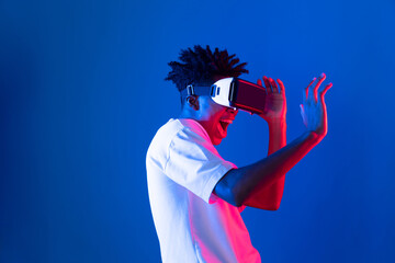 Surprised young African American looking through VR holding interesting object hologram on pink...