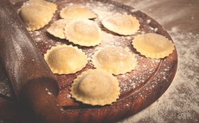 fresh raw, uncooked ravioli, on a cutting board, with a rolling pin for dough, wooden background, no people,