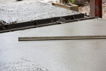 Construction worker spreading wet concrete pouring at precast concrete wall construction site. Worker or mason working or making smooth surface of concrete at site work