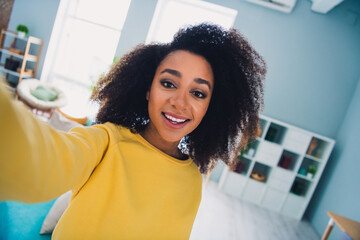 Photo of positive cheerful lady dressed yellow sweatshirt smiling tacking selfie indoors house room