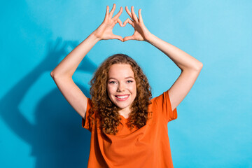 Photo of youngster happy lady in orange t shirt showing heart symbol above head support charity donation isolated on blue color background