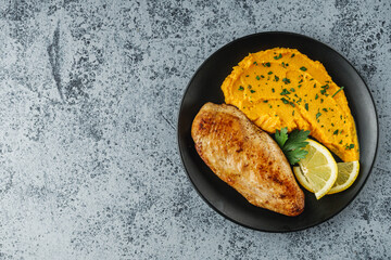 delicious mashed sweet potatoes and fried chicken breast on a light stone background