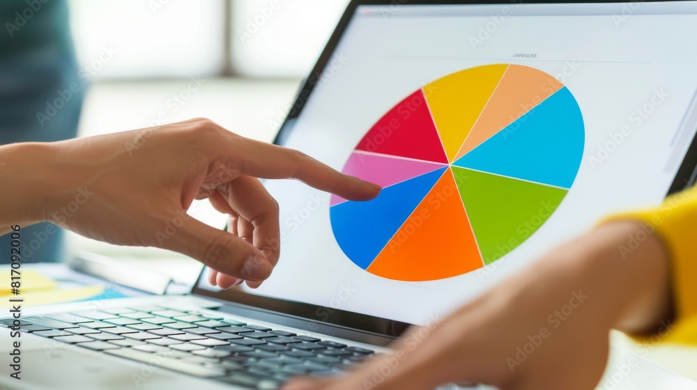 Poster hands pointing at a colorful pie chart on a laptop screen during a collaborative discussion.