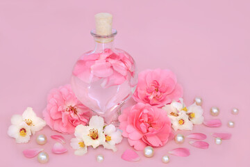 Rose and orange blossom flower perfume in heart shaped bottle on pink with loose flowers and pearls. Floral beauty product, gift for Valentines Day, birthday, anniversary or Mothers day.