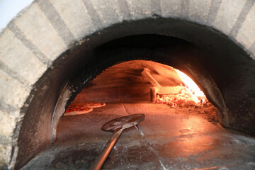 Italian pizzas cooking in a wood-fired oven with a metal shovel for retrieving them