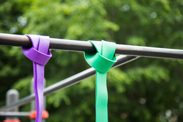 Purple and green Elastic rubber bands for exercise tied on a horizontal bar . Horizontal shot ....