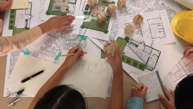 Architect and engineer consider or discuss about building construction using blueprint on table with architectural document, measurement tool and wooden block scatter around at office. Delineation.