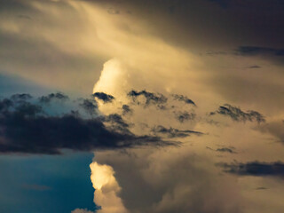 Foreground cloud and cloudlets in silhouette, with larger clouds in the distance illuminated by the...