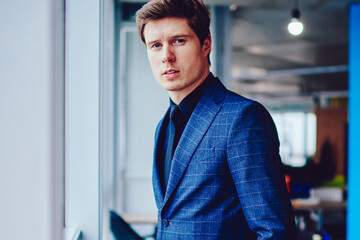 Portrait of elegant caucasian businessman looking at camera while waiting colleague in company office, stylish serious male entrepreneur in trendy suit spending time in workspace before conference