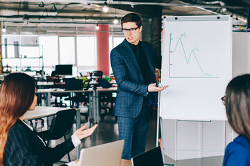 Serious male speaker standing near flip chart and making brainstorming during productive...