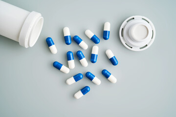 Blue and white capsules spilled out of a medicine jar on a blue background.