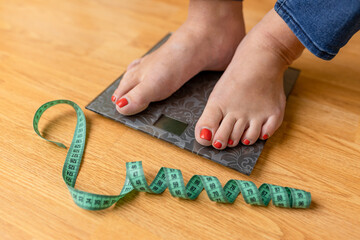 A picture of female feet standing on a floor scales and a tape measure. Close-up