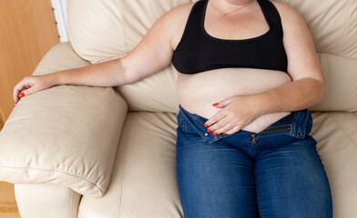 Depressed overweight woman sitting on sofa at home. Diet concept