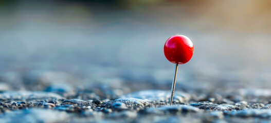 A red pin is stuck in the ground on a grey surface. The pin is the only object in the image, and it...