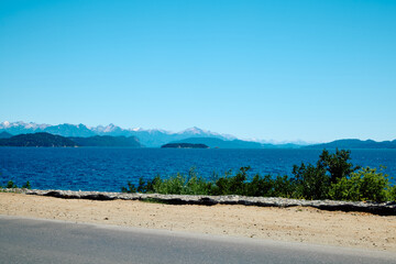 road with bushes near a blue lake against the backdrop of rocky mountains