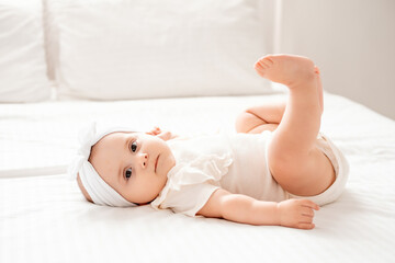Cute newborn baby girl playing with her legs lying on her back o